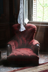 Red armchair in an abandoned room with light beams from the brocken window