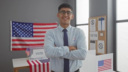 Young man with 'i voted' sticker stands confidently in a polling station with american flags.