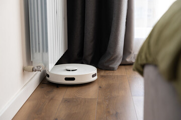 A white robot vacuum cleaner with a sweeping brush, infrared motion sensors and a camera cleans the...
