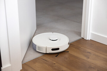 A white robot hoover cleans tiles and wooden floors through the threshold without obstacles....