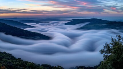  A picturesque mountain range shrouded in clouds during sunset, with a vivid pink and blue sky in the backdrop
