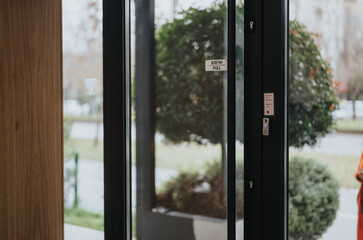 View through a contemporary glass door marked with pull signs and equipped with electronic access control panels on a bright day.