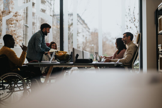 An inclusive modern office environment with professionals collaboratively working. A man in a wheelchair actively participates in a business meeting.