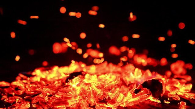 Hot smoldering embers in the campfire. Close up view on the glowing charcoals and tiny sparkles going up.