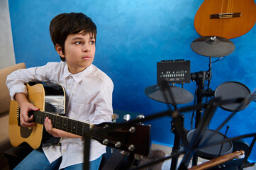 Authentic portrait of an adolescent boy playing guitar in the modern music studio. Electric guitar...