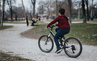 A boy enjoys cycling on a gravel path in a city park, surrounded by lush greenery and breathing fresh air.