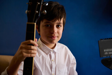 Authentic portrait of a teenager boy guitarist, young talented musician holding acoustic guitar,...