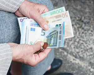 Euro banknotes and coins in the hands of an elderly woman.	
