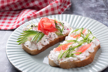 Bruschetta, a slice of bread with cheese paste, tomato and cucumber. Beautifully decorated sandwiches on a plate