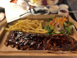 Barbecue Grilled Pork Ribs with French Fries and Salad on Wooden Plate in a restaurant