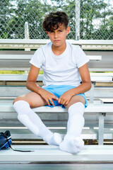 Youth male soccer player sitting on bleachers with his cleats off before a game