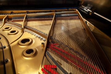 Inside of a small baby grand piano with strings and brass coloring