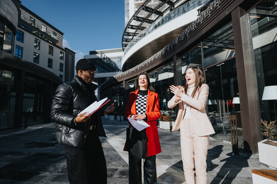 Three diverse colleagues share a moment of success and happiness outside a modern office building in a sunny environment. - Powered by Adobe