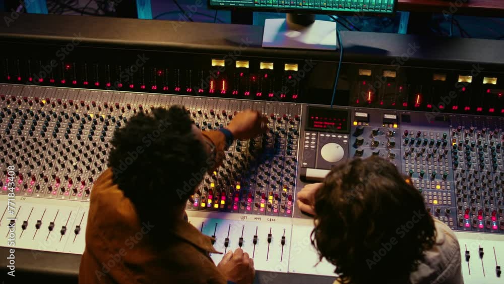 Poster Music production team examining volume levels on audio software, using mixing and mastering techniques to create a hit song. Musician and sound designer work on editing recorded tracks. Camera B.