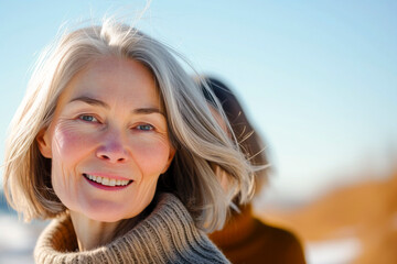 A woman with gray hair is smiling and wearing a sweater