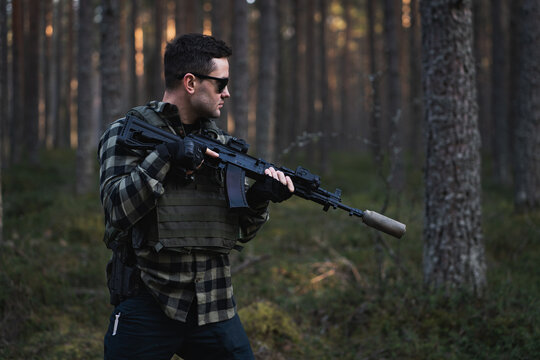 Male private military man with a modern assault rifle and body armor in the forest.