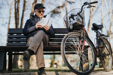 Senior man enjoying leisure time with tablet in park, bike by side.