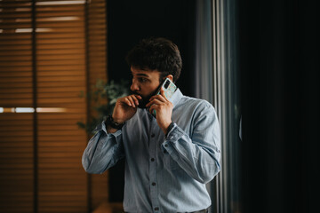 A focused business entrepreneur in a casual shirt engaged in a serious phone conversation - obrazy, fototapety, plakaty