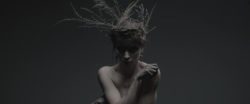 A sorceress dressed as mother nature on a dark studio background performs dance-like ritual