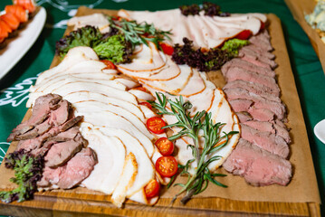 Assorted Cold Meat Platter with Fresh Herbs. A delectable array of cold meats, including sliced turkey and roast beef, garnished with fresh herbs and cherry tomatoes.