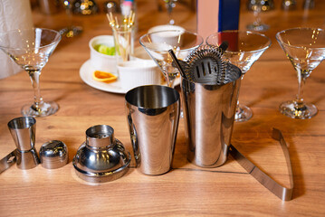 Professional Bartender Toolkit on Wooden Bar. Stainless steel bartender tools neatly arranged on a wooden bar top, including shakers, jiggers, and strainers.