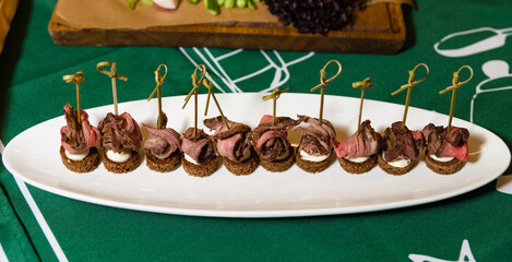 Roast Beef Appetizers with Cream Cheese on Pumpernickel. Savory roast beef slices on cream cheese and pumpernickel bread, garnished with fresh herbs for an elegant hors d'oeuvre. - obrazy, fototapety, plakaty