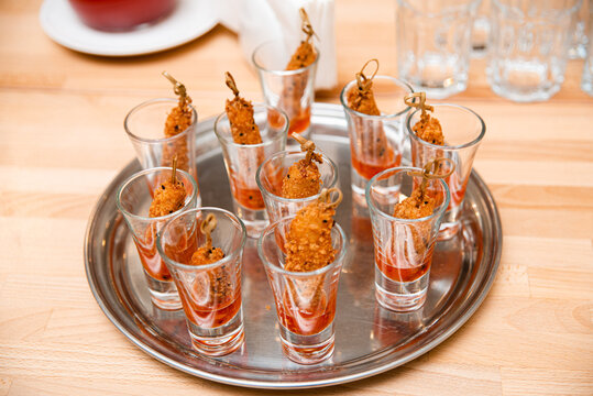 Crispy Shrimp Appetizers in Shot Glasses with Sauce. Shot glasses filled with sweet spicy sauce and topped with crispy fried shrimp, presented on a silver tray for a stylish catering event.