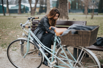 Confident young businesswoman taking a break outdoors, exuding elegance and style while sitting on a park bench beside a bicycle.