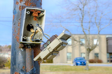 A broken electrical panel on the side of an outdoor pole. The front is hanging off, held to the box...