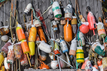 Many fishing buoys hanging from the side of a faded wooden building. These are the type of buoy...