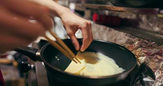 Cooking, chopsticks and person with egg in pan at market for frying food for meal preparation, eating and nutrition. Culinary, flame and closeup of chef prepare lunch, cuisine dinner and supper