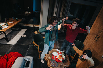 Top view of happy young adults dancing and enjoying a casual indoor party with drinks and snacks on the table.