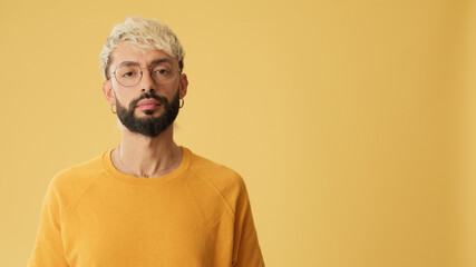 Obraz premium Guy with glasses, dressed in yellow T-shirt, looking at camera, isolated on yellow background in studio