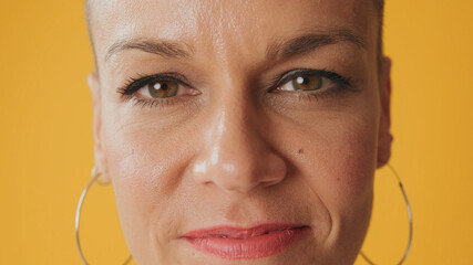 Close-up portrait of young happy hairless woman opening her eyes looking at camera isolated on yellow background in studio