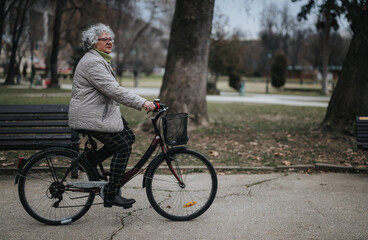 A mature retiree finds joy and vitality riding her bike among the serene park scenery
