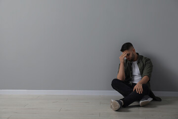 Sad man sitting on floor near light grey wall. Space for text