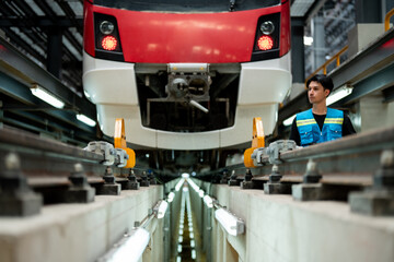 A focused technician with a tablet is inspecting a modern train in an industrial maintenance...