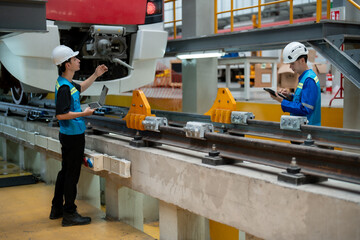 A focused technician with a tablet is inspecting a modern train in an industrial maintenance...