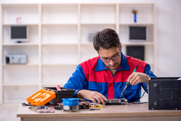 Young male repairman repairing computer - obrazy, fototapety, plakaty