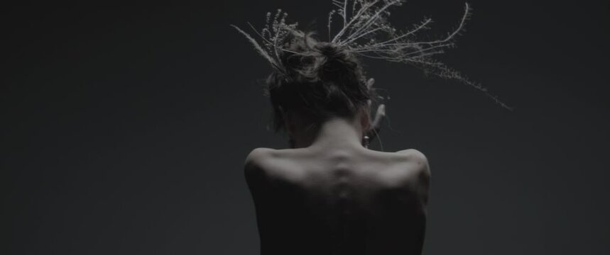 A skinny model dressed like mother nature performs a ritual dance in a studio 