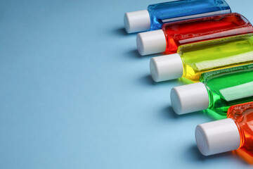 Fresh mouthwashes in bottles on light blue background, closeup. Space for text