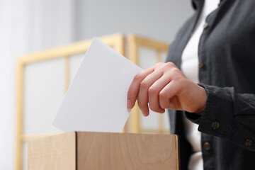 Woman putting her vote into ballot box on blurred background, closeup