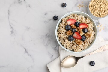 Tasty oatmeal with strawberries, blueberries and walnuts served on white marble table, flat lay. Space for text