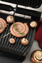 Electric grill with homemade sausages, rosemary and mushrooms on marble table, above view