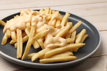 Delicious french fries with cheese sauce on wooden table, closeup