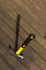 A multi-purpose hammer with a yellow and black handle resting on its head on an acacia wood plank surface