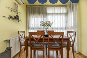 cherry wood dining table with matching blue upholstered chairs and a large window with white curtains
