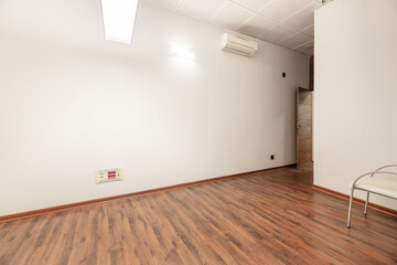 A small empty office with an armchair with white seats and a reddish floor