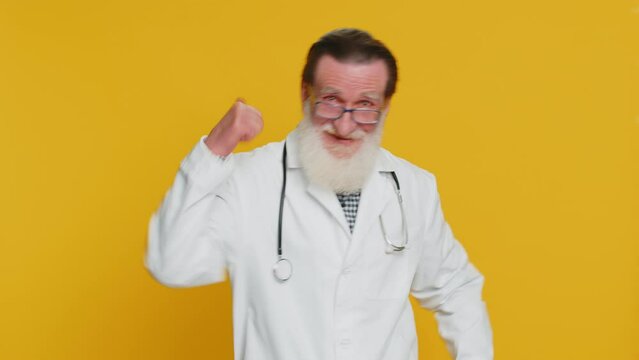 Like. Senior elderly doctor cardiologist man raises thumbs up agrees, gives positive reply good idea feedback celebrating success victory. Apothecary pharmacy grandfather isolated on yellow background