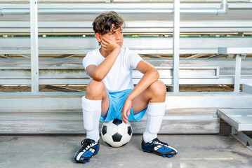 Youth male soccer player sitting on a soccer ball waiting for his chance to play the game